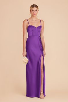 a woman in a long purple dress with a slit down the side, holding a bouquet