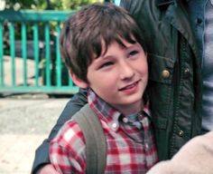 a young boy is holding his backpack and smiling at the camera while standing next to an adult