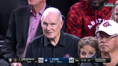 an old man sitting in the stands at a basketball game with other people behind him