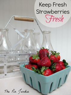 a blue bowl filled with strawberries on top of a table next to glass bottles