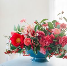 a blue vase filled with red and pink flowers on top of a table next to a window