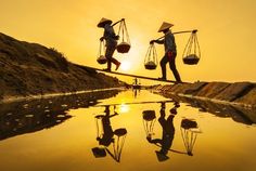 two people walking across a body of water with bags on their backs and one carrying something in the other hand