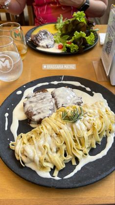 a plate with some meat and noodles on it next to a glass of water at a table