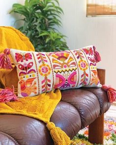 a brown leather chair with two colorful pillows on it and a plant in the background