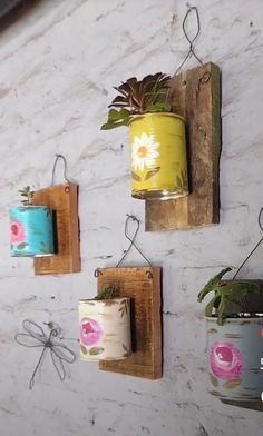 three tin cans are hanging on the wall with plants in them and one has a planter attached to it