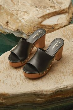 The Lulus Jaylani Black Platform Mule Sandals are the perfect combination of cute and cool for all your warm weather 'fits! Smooth faux leather shapes these essential sandals that have an almond footbed and a wide vamp strap with shiny gold stud accents along the side, all atop a 1.25"" toe platform. Easy slide-on design makes for effortless, everyday styling, while a sturdy wood-look block heel completes the classic clog-inspired look! 3. 75" wood-look block heel. Lightly cushioned insole. Rubb Chic Synthetic Clogs With Open Heel, Summer Synthetic Clogs With Stacked Heel, Chic Open Toe Clogs With Cushioned Footbed, Chic Clogs With Wooden Heel For Beach, Chic Beach Clogs With Wooden Heel, Beach Clogs With Block Heel In Synthetic, Chic Block Heel Clogs For The Beach, Chic Beach Clogs With Block Heel, Summer Synthetic Clogs With Heel Strap