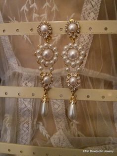 two pairs of pearl and crystal earrings on display in a store window, with lace behind them