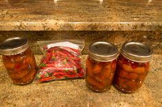 three jars filled with pickles sitting on top of a counter next to a bag