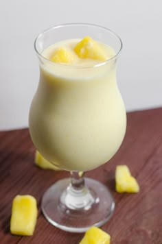 a glass filled with pineapple whip margarita on top of a wooden table