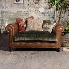 a brown leather couch sitting in front of a brick wall with potted plants next to it