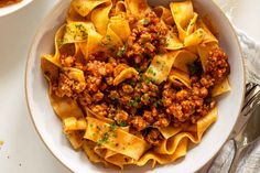 a white bowl filled with pasta and meat on top of a table next to silverware