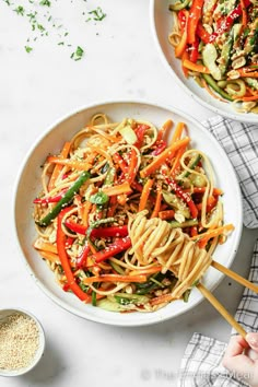 two bowls filled with noodles and vegetables on top of a white countertop next to a wooden spoon