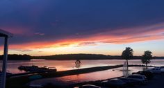 the sun is setting over a body of water with cars parked on it and trees in the background