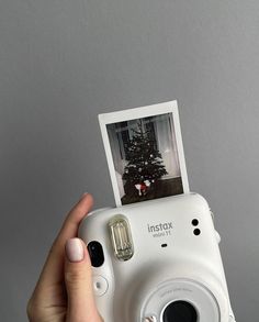 a person holding up a white camera with a christmas tree on the top and an instax film attached to it