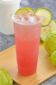 a pink drink with limes and ice on a cutting board