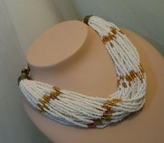 35 strands of handstrung white and gold seed beads adorned in a choker fashion.  Like New condition White Multi-strand Large Beads Jewelry, White Multi-strand Beaded Necklaces, White Multi-strand Beaded Necklace, White Multi-strand Necklace With Gold Beads, White Multi-strand Large Beads, White Large Multi-strand Beads, Vintage White Multi-strand Beaded Necklaces, White Multi-strand Beaded Necklace With Large Beads, White Multi-strand Jewelry With Tiny Beads