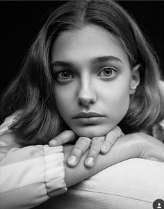 a black and white photo of a woman with her hand on her chin looking at the camera