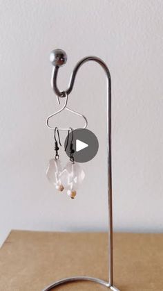 a pair of earrings is hanging from a metal stand on a table with a white wall in the background