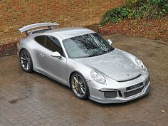 a silver porsche parked in front of a brick wall