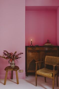 a pink room with two chairs and a vase filled with flowers next to a dresser