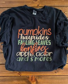 "Pumpkins Hayrides Falling Leaves Bonfires, Fall Shirts, Gildan Unisex Shirt, Hello Fall Shirt, Welcome Fall Shirt, Glitter Fall Shirt --------------------------------------------------------------------------------------------------------------------- Design colors (Glitter Orange, Glitter Copper, and Olive Green) as shown in the pictures. You can get this in a long sleeve or short sleeve.  HOW TO ORDER: 1. Select the Shirt Size and Long or Short Sleeve 2. Select the Shirt Color. 3. Select the Fun Short Sleeve Tops For Fall, Fun Fall Graphic Print Shirt, Fun Graphic Print Fall Shirt, Fall Graphic Tee With Text Print, Fall Graphic Tee Shirt With Text Print, Fun Graphic Print Shirt For Fall, Black Text Print Shirt For Fall, Fun Fall Shirt With Letter Print, Reserved Wedding Signs