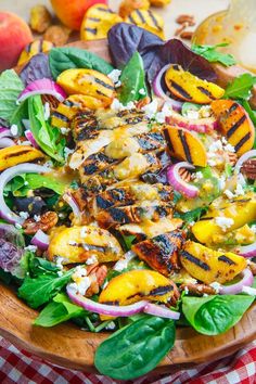 a salad with grilled chicken, onions and spinach in a wooden bowl on a checkered tablecloth