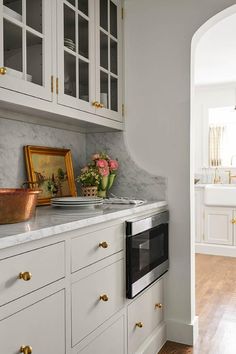 a kitchen with white cabinets and marble counter tops, gold handles on the oven door