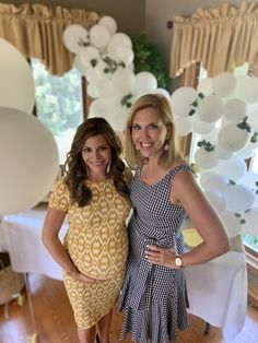 two women standing next to each other in front of white balloons and table cloths