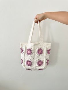 a hand holding a white crocheted bag with pink flowers