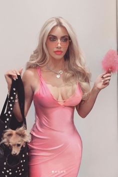 a woman in a pink dress holding a black bag and a small dog on her shoulder