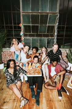 a group of people sitting on top of a wooden floor next to each other in front of a pizza box