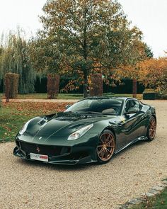 a black sports car parked on top of a gravel road in front of some trees