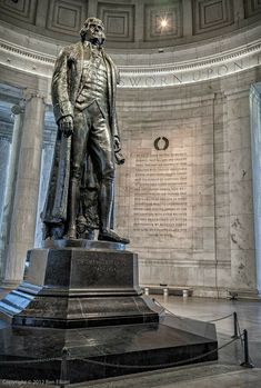 there is a statue in the center of this building that has writing on it and an oval ceiling