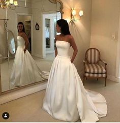 a woman standing in front of a mirror wearing a white wedding dress and looking at her reflection