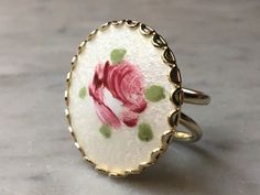 "This large vintage statement ring is decorated with a hand painted pink rose on white guilloche enamel. Set in gold tone metal, the white circle front has small swirl patterns in the enamel. The ring has a double band and fits comfortably on one's finger. Size: US Size 5 1/4. The ring is 1 1/8\" in diameter. This item weighs 9.2 oz. This item is in great vintage condition! There are no missing pieces or damages. Please feel free to contact us with any questions you may have about this item! **W Formal White Jewelry With Rose Design, Formal White Rose Design Jewelry, Vintage White Hand Painted Jewelry, Vintage Hand Painted White Jewelry, Handmade White Enamel Ring, Elegant Hand Painted Enamel Ring, Hand Painted White Jewelry For Wedding, Vintage Hand Painted Pink Jewelry, White Oval Enamel Ring Gift