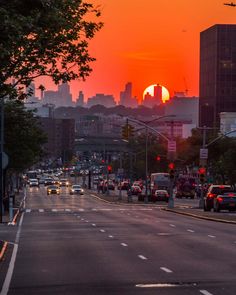 the sun is setting over a city street with cars driving on it and buildings in the background