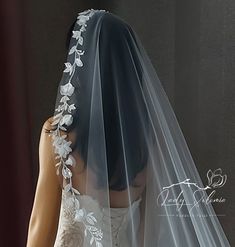 the back of a bride's veil with flowers and leaves on it is shown