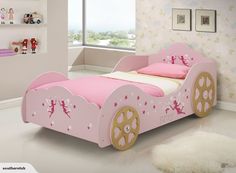 a child's pink bed with gold wheels and stars on the side, in a white room