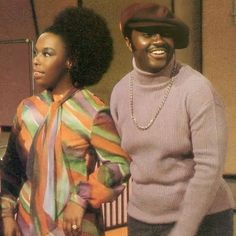 two black women standing next to each other in front of a table and chairs with one woman wearing a colorful sweater