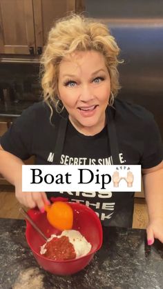 a woman in black shirt holding a red bowl filled with food and pointing at the camera