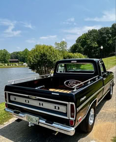 an old black truck parked on the side of a road next to a body of water