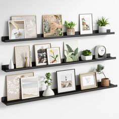 three black floating shelves with pictures and plants on them, along with other decorative items