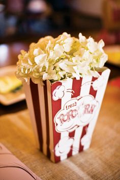 a popcorn box filled with white flowers sitting on top of a table