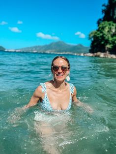 a woman in the water wearing sunglasses and smiling at the camera while floating on her stomach