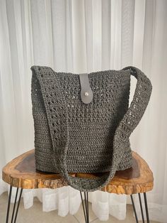 a gray crocheted bag sitting on top of a wooden table next to a white curtain