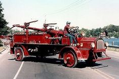 an old fire truck driving down the road with a man sitting on it's back