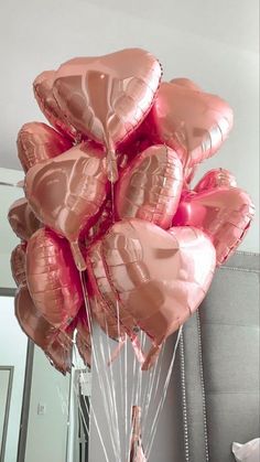 a bunch of pink heart shaped balloons in a room with a mirror and bed behind it