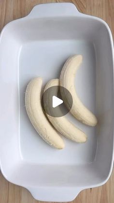 two peeled bananas in a white bowl on a wooden table with a video play button