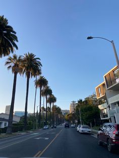 cars are driving down the street in front of palm trees and apartment buildings on a sunny day