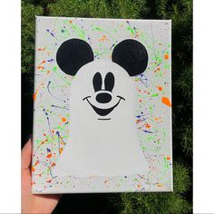 a hand holding up a mickey mouse painted on canvas with paint splattered all over it